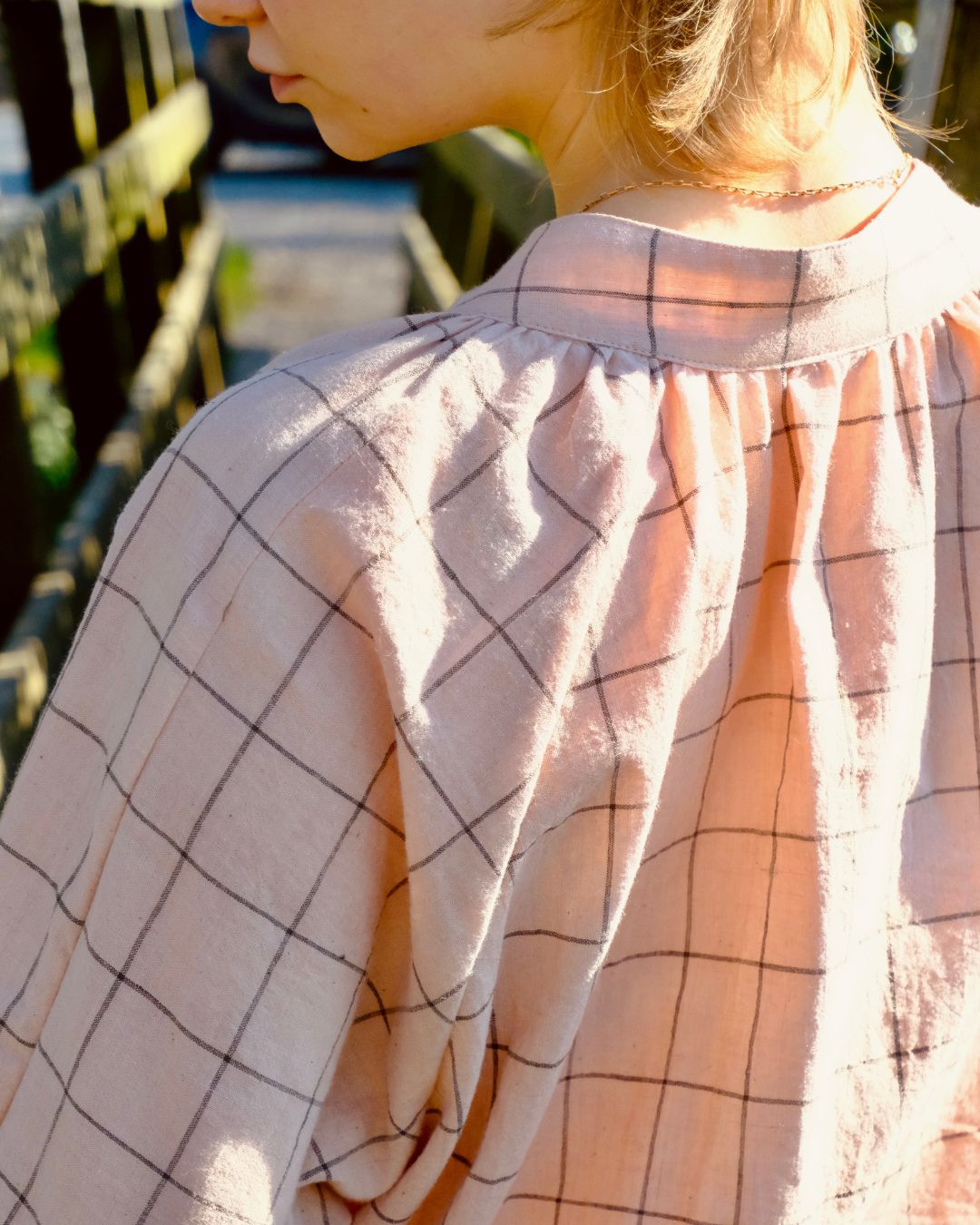 Person wearing a light pink shirt with black grid pattern outdoors