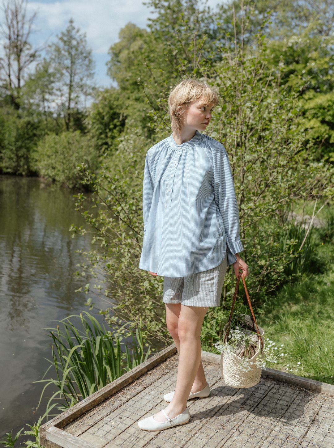 Woman standing on a wooden platform by a pond with greenery in the background