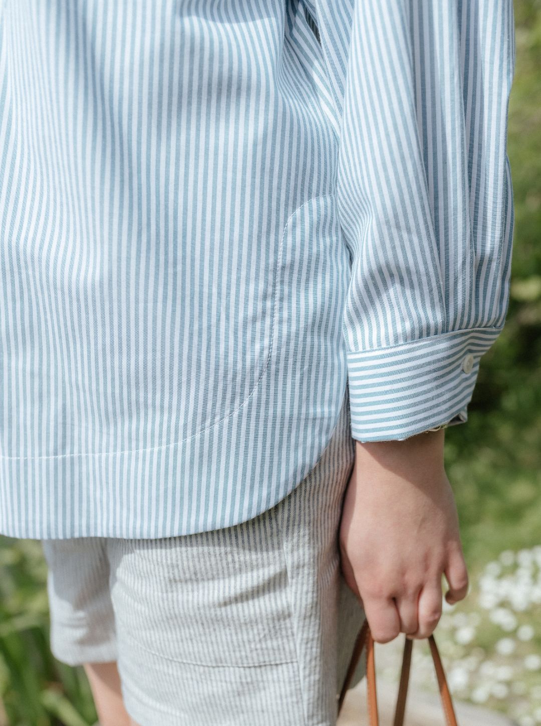Person wearing a light blue and white striped shirt with rolled-up sleeves, standing outdoors.