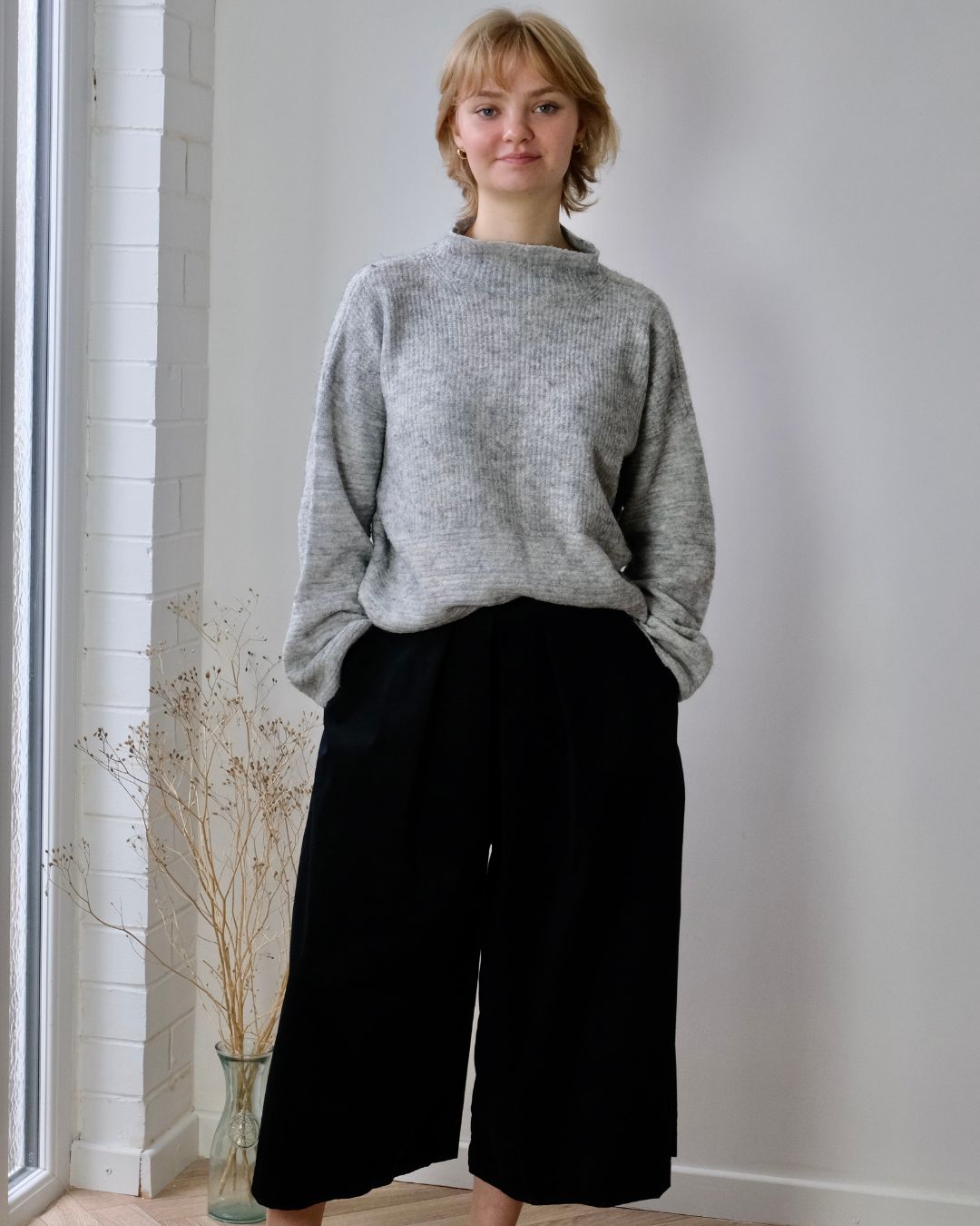 woman standing in studio wearing grey jumper and black needlecord culottes