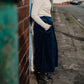 Person wearing a striped sweater and navy skirt standing against a wall on a street.
