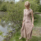 Woman in a checkered dress standing by a body of water with greenery.