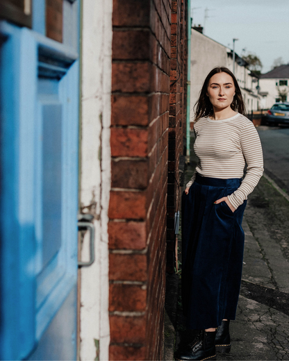 a person stood outside a blue door on a street wearing stripe top and blue cord culottes