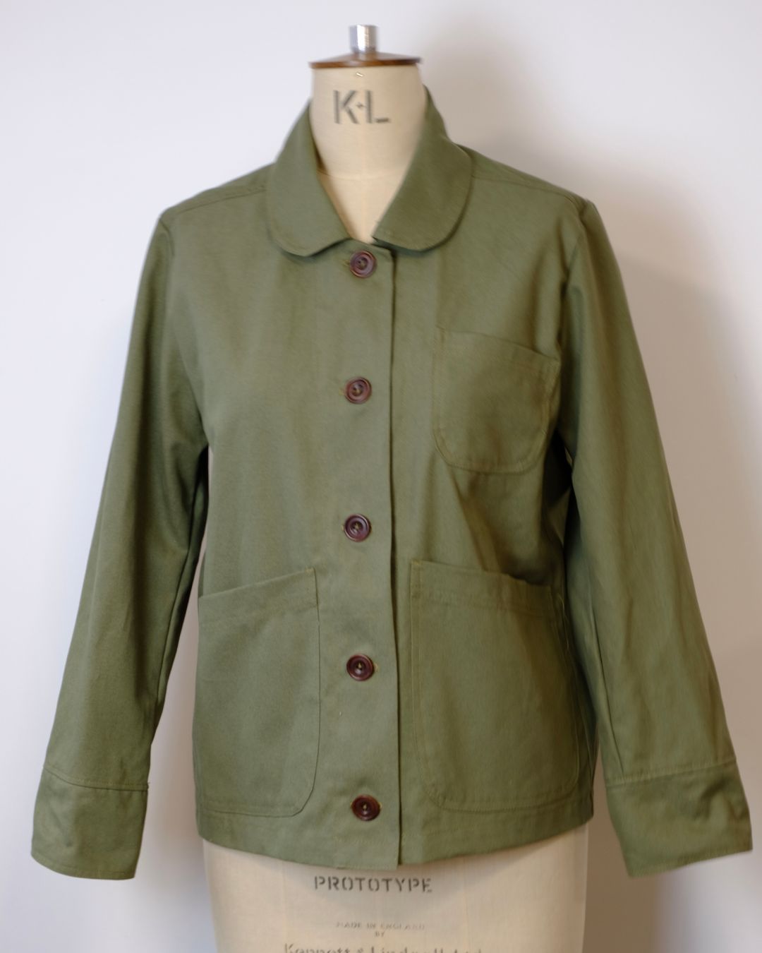 Green jacket on a mannequin with 'K-L' branding against a white background