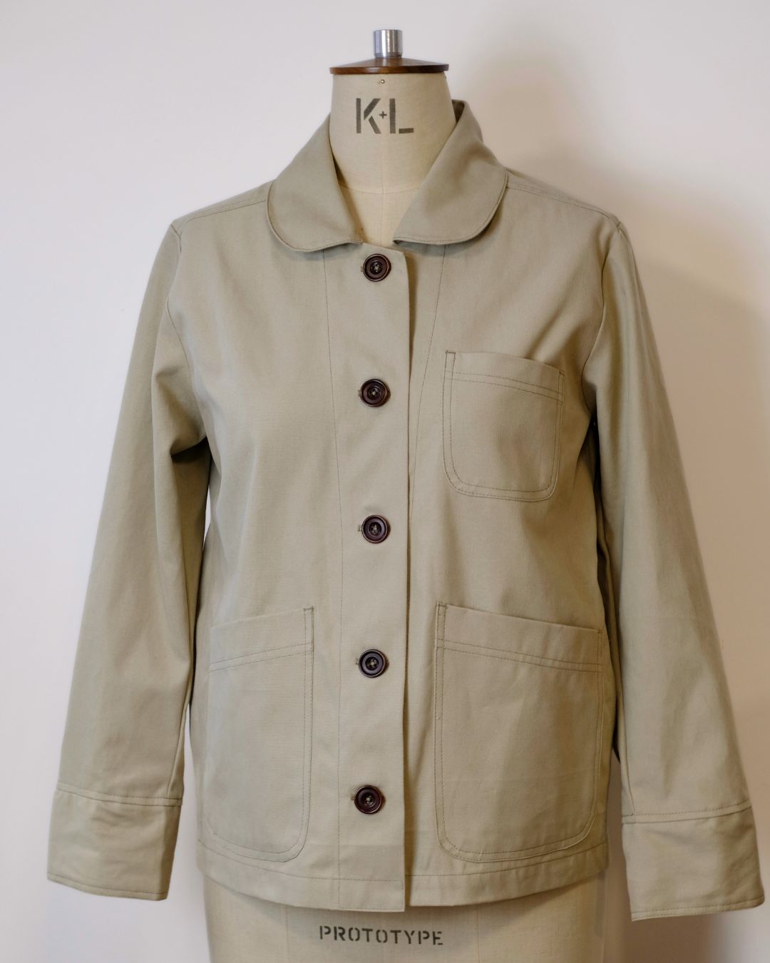Beige jacket on a mannequin with 'K.L' branding against a white background