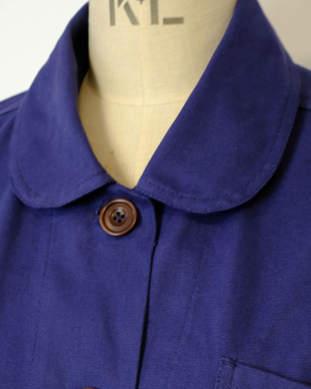Close-up of a blue garment with a brown button on a mannequin.