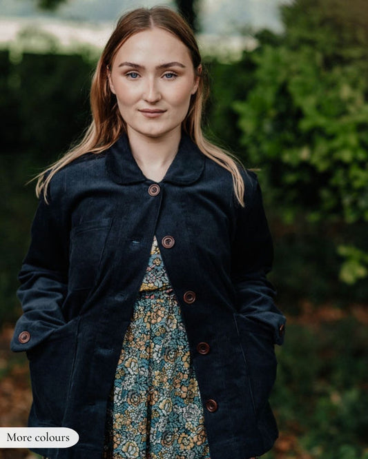 Woman wearing a dark coat over a patterned dress with a blurred green background