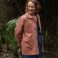 Woman wearing a pink jacket standing in a natural setting with greenery.