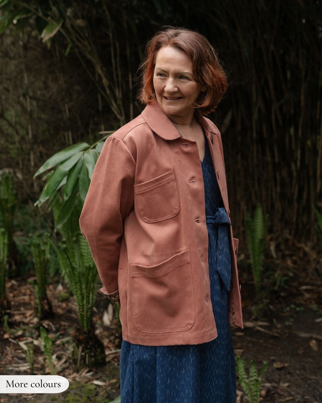 Woman wearing a pink jacket standing in a natural setting with greenery.