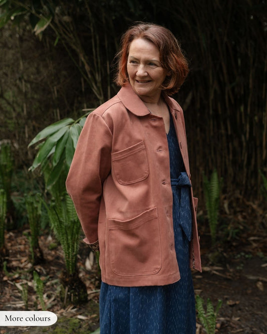 Woman wearing a pink jacket standing in a natural setting with greenery.