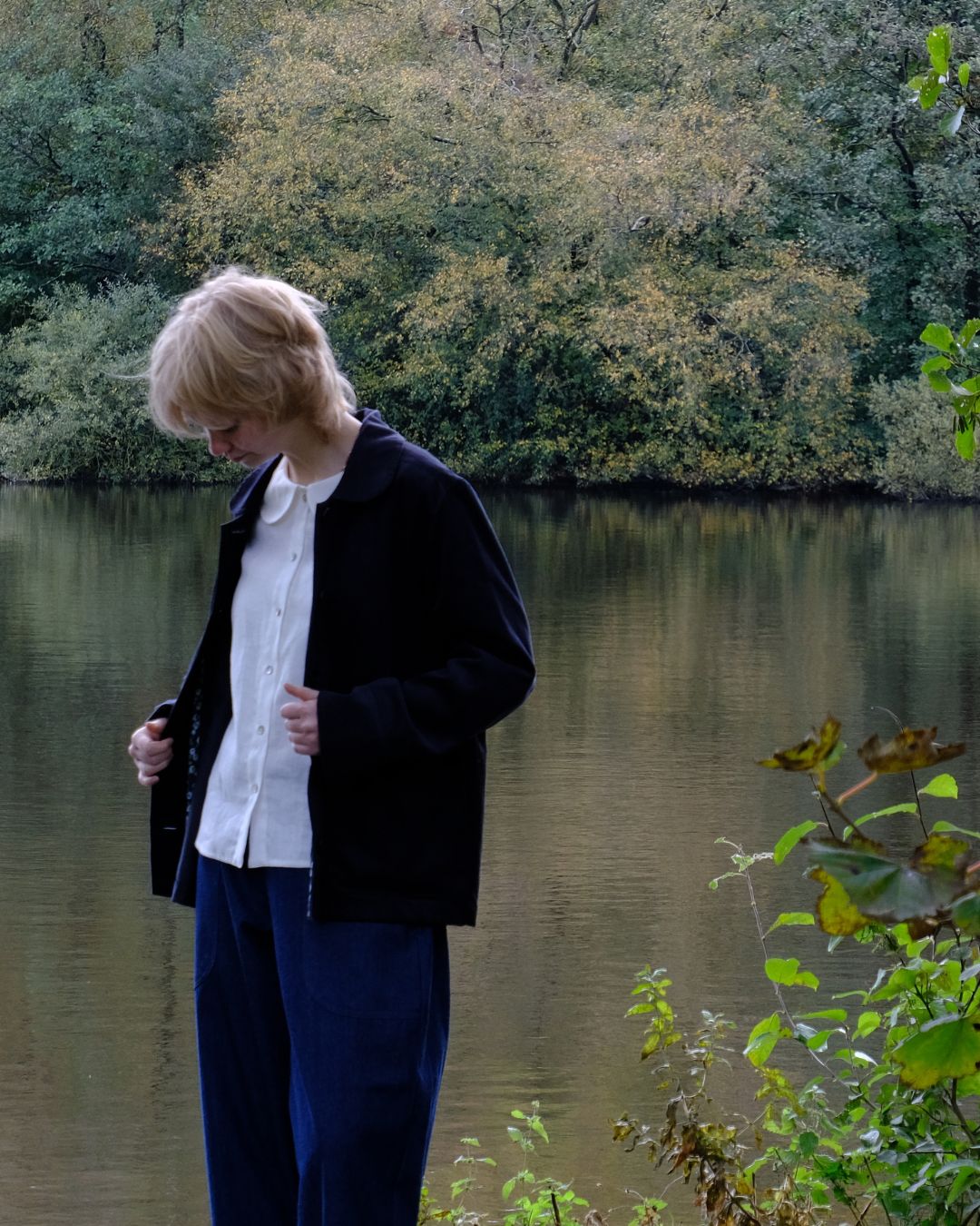 Person standing by a body of water with trees in the background