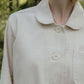 Close-up of a beige shirt with buttons and collar against a blurred natural background