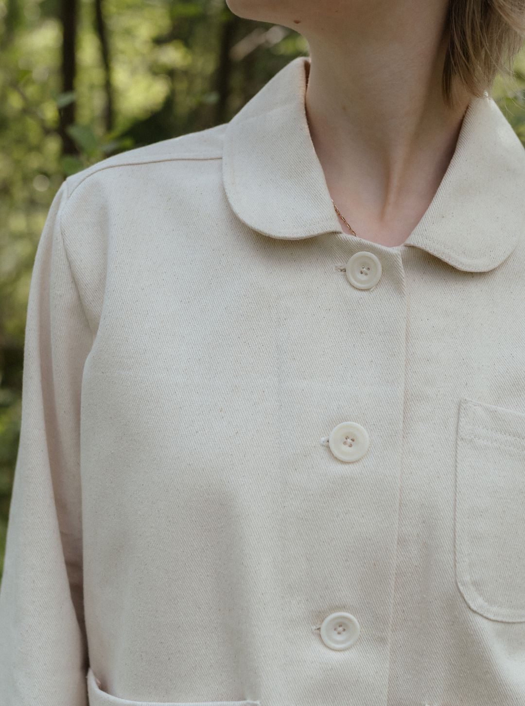 Close-up of a beige shirt with buttons and collar against a blurred natural background