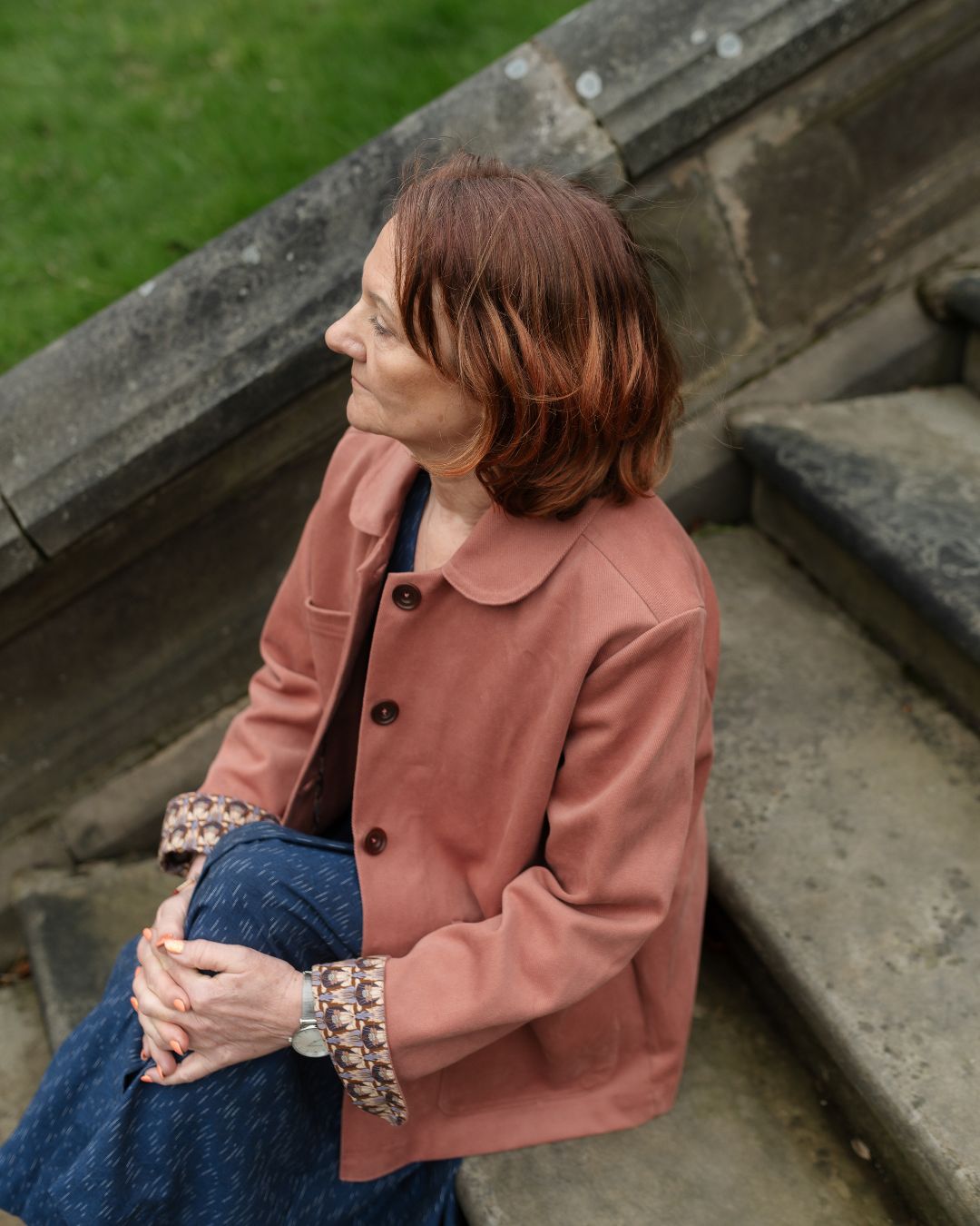 woman sitting on steps outside wearing pink jacket