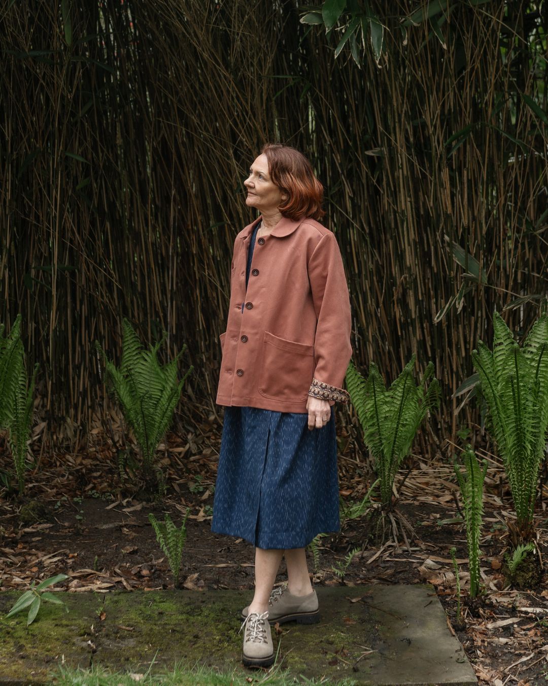 woman standing in garden wearing pink jacket.