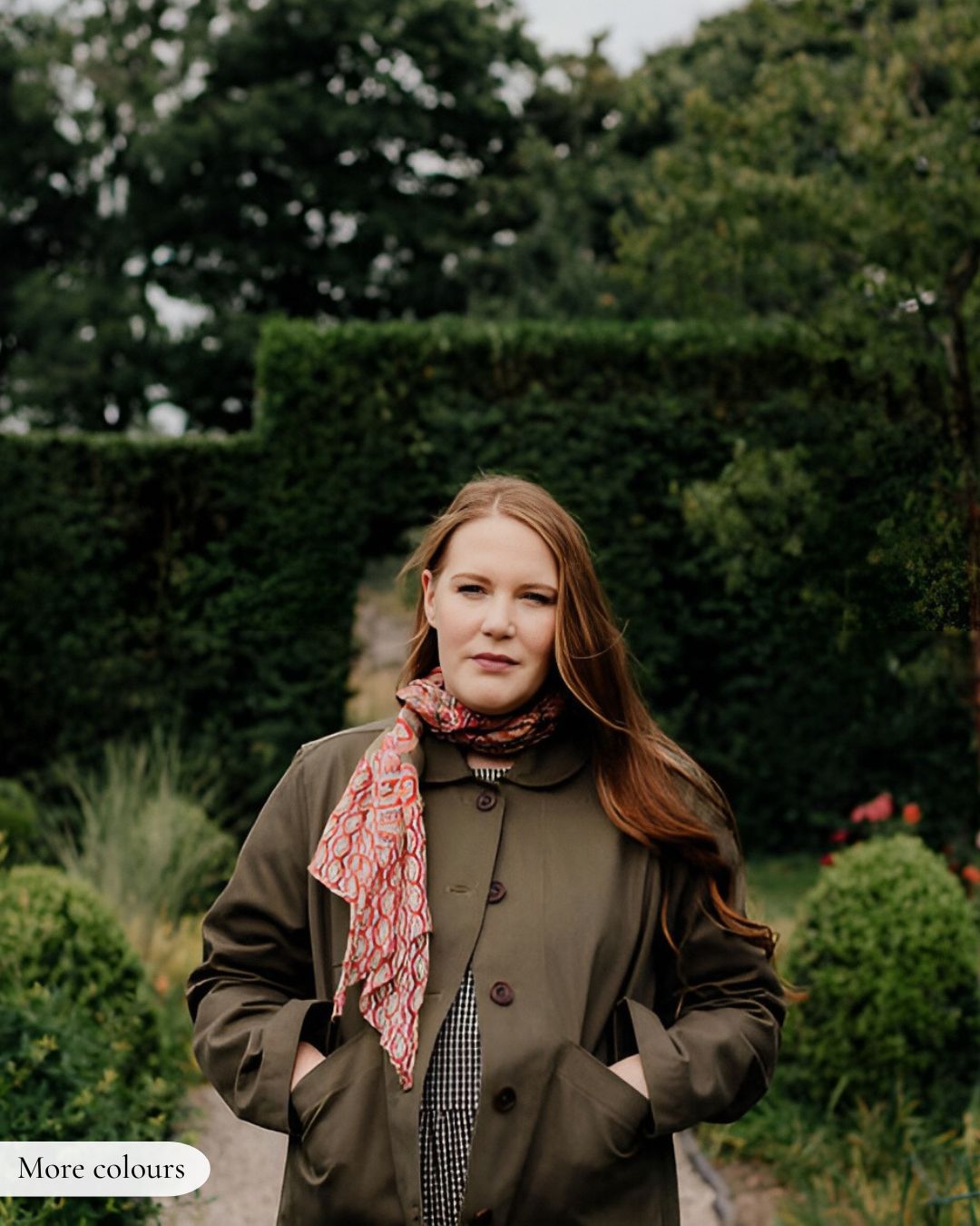 Woman wearing a green coat and red scarf in a garden setting