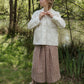 Woman in a white jacket and checkered skirt standing in a natural setting with trees and water.