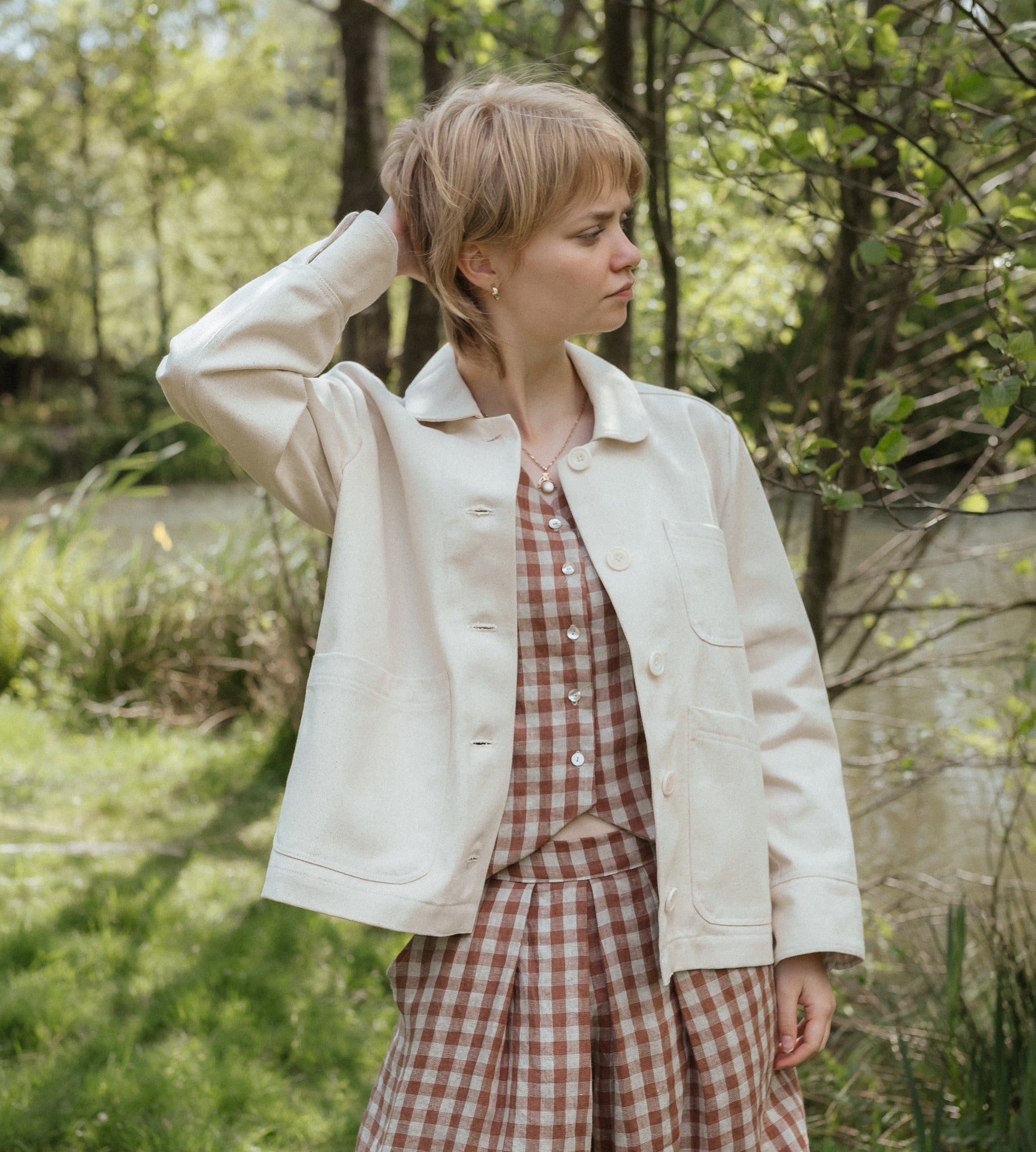 person wearing white jacket with greenery in background.