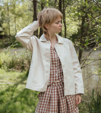 person wearing white jacket with greenery in background.