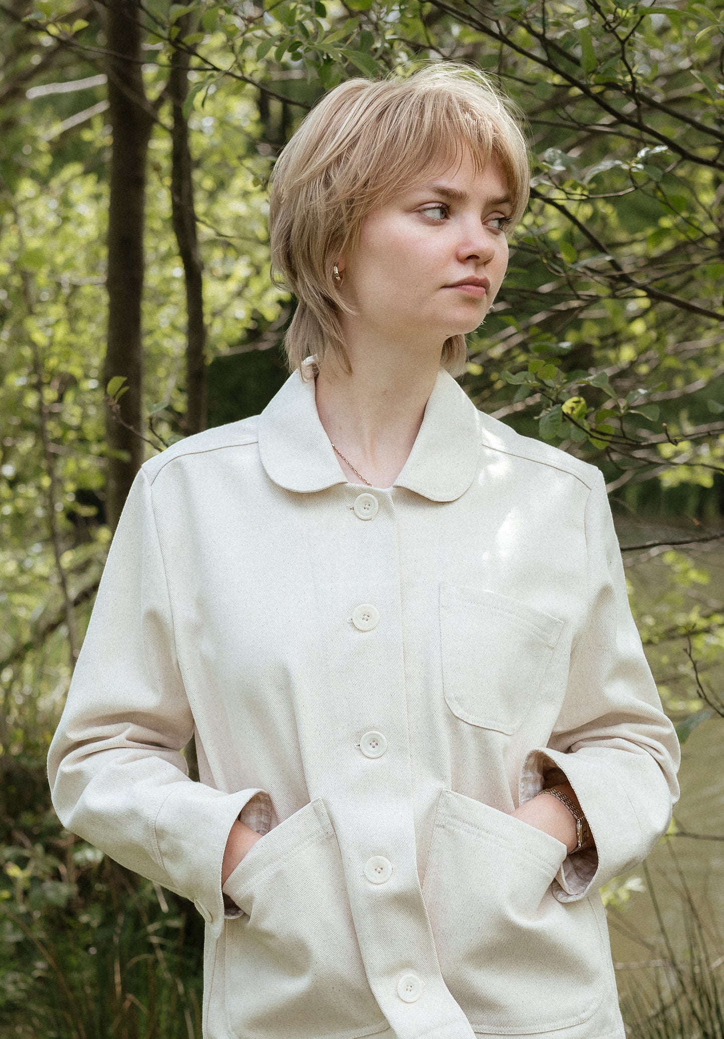 Person standing in countryside wearing a white jacket with hands in pockets.