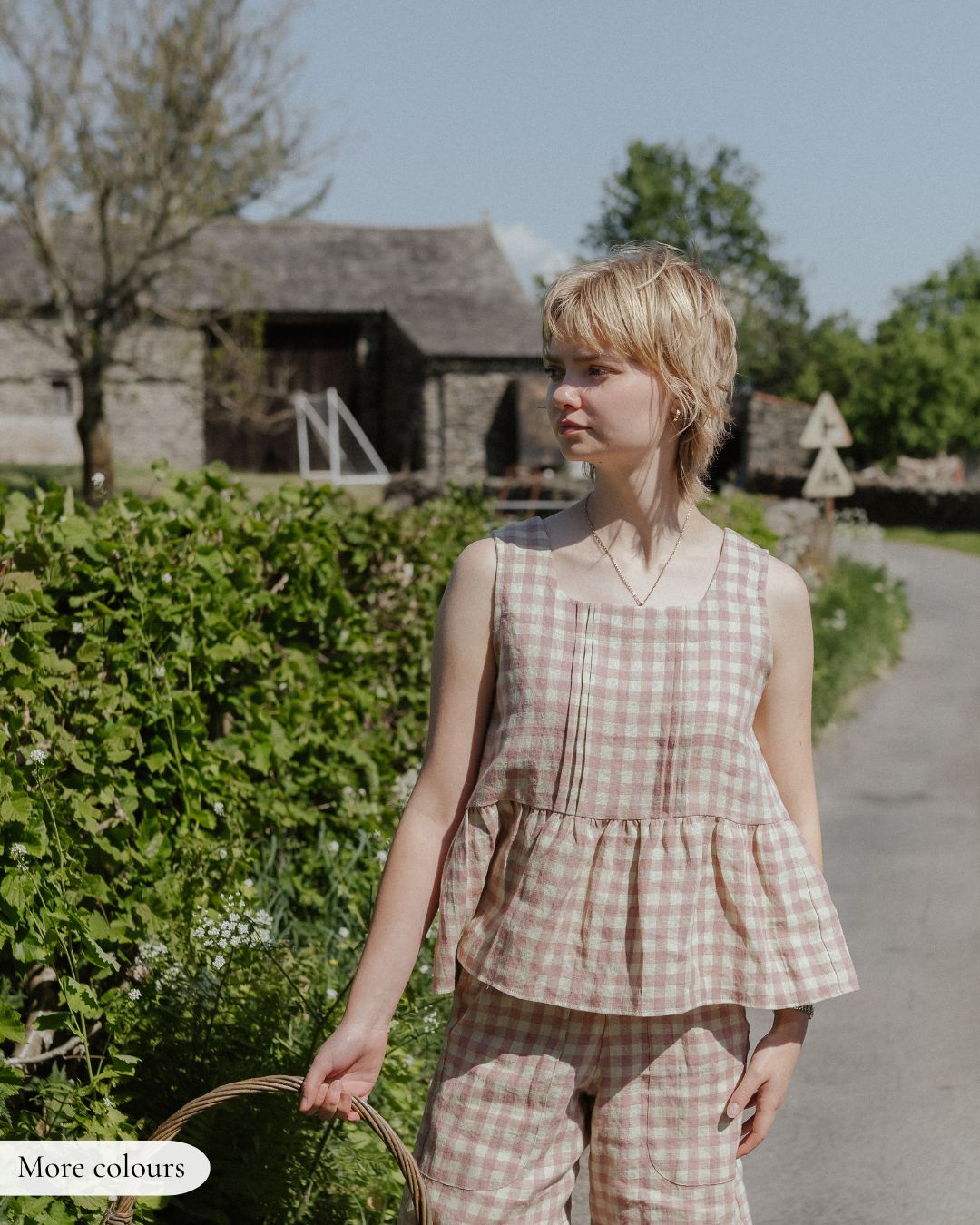 Young girl in a checkered outfit standing on a path with greenery and a building in the background