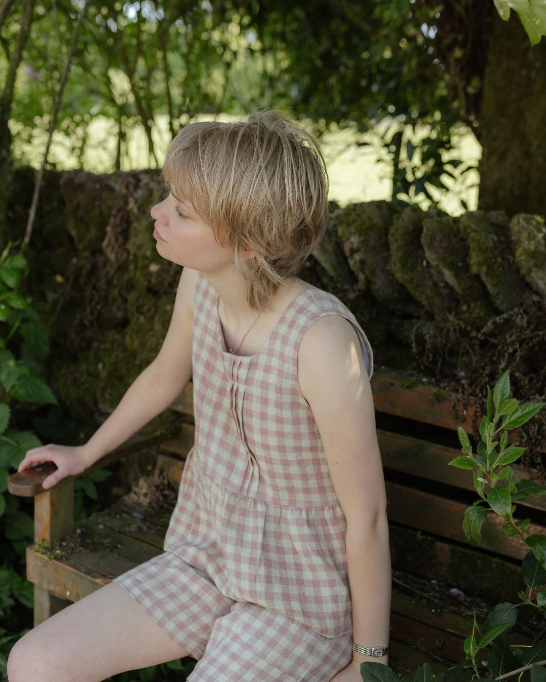 Woman in a checkered outfit sitting outdoors with greenery around
