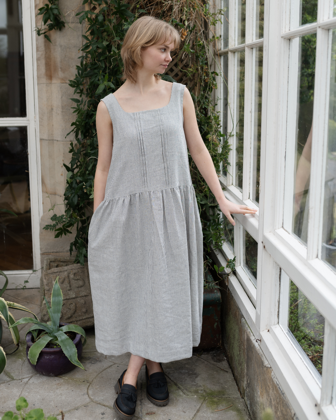 a woman standing in conservatory wearing stripe pinafore dress with pockets