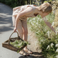 Woman in a checkered dress picking flowers by a stone wall