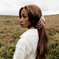 Woman wearing a cream linen blouse  standing holding hair in a moorland setting