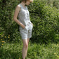 Woman wearing a gray sleeveless top and shorts standing in a natural setting with greenery.
