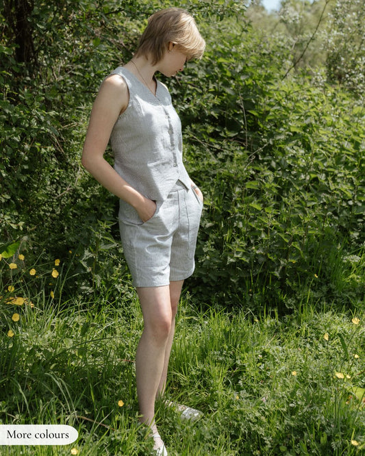Woman wearing a gray sleeveless top and shorts standing in a natural setting with greenery.
