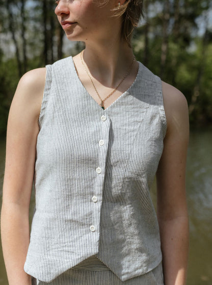 Woman wearing a sleeveless button-up shirt outdoors with greenery in the background