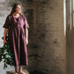 Woman in a maroon dress holding greenery in a rustic room.