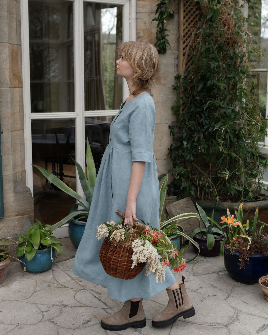 Woman wearing blue dress in a conservator holding a basket of flowers