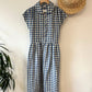 Blue and white checkered linen  dress with a straw hat on a white wall.
