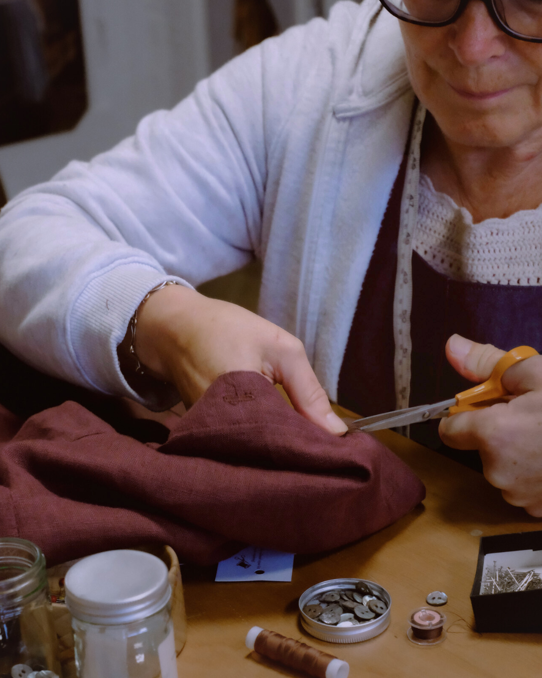 Person cutting fabric with scissors on a table with various items