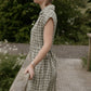 Woman in a checkered dress standing on a wooden bridge in a natural setting