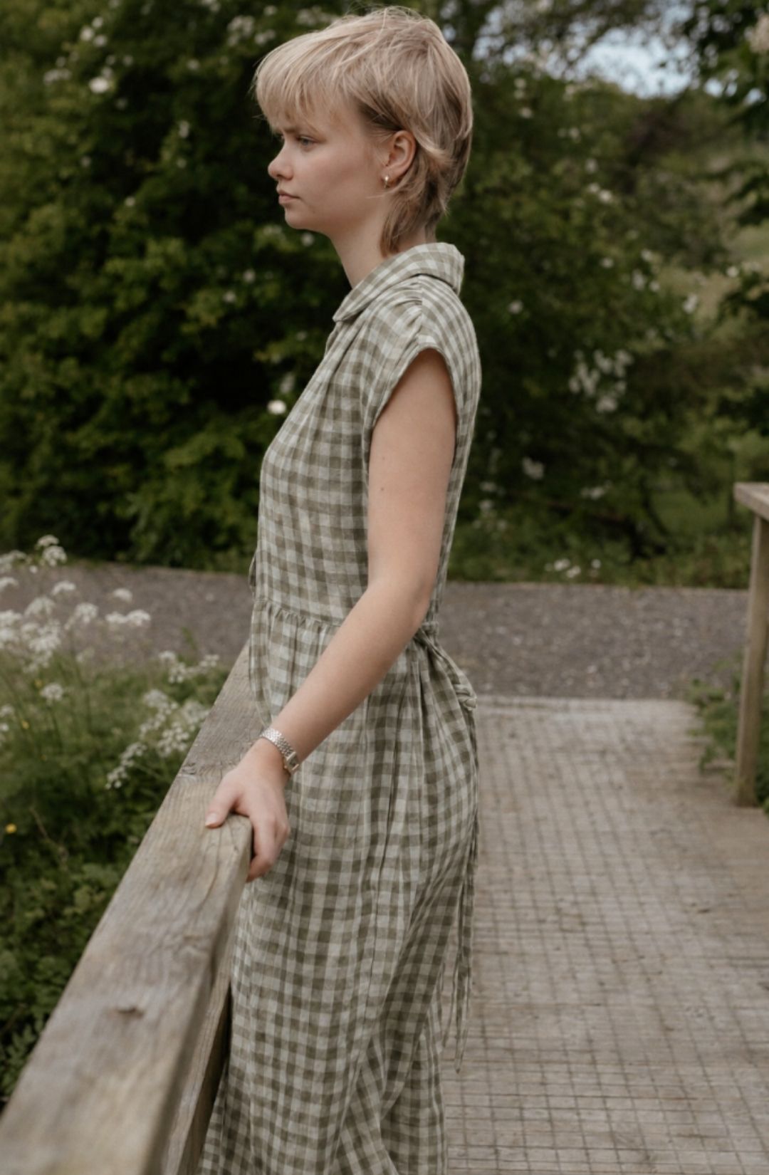 Woman in a checkered dress standing on a wooden bridge in a natural setting