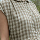 Close-up of a sleeveless checkered dress with buttons on a blurred natural background