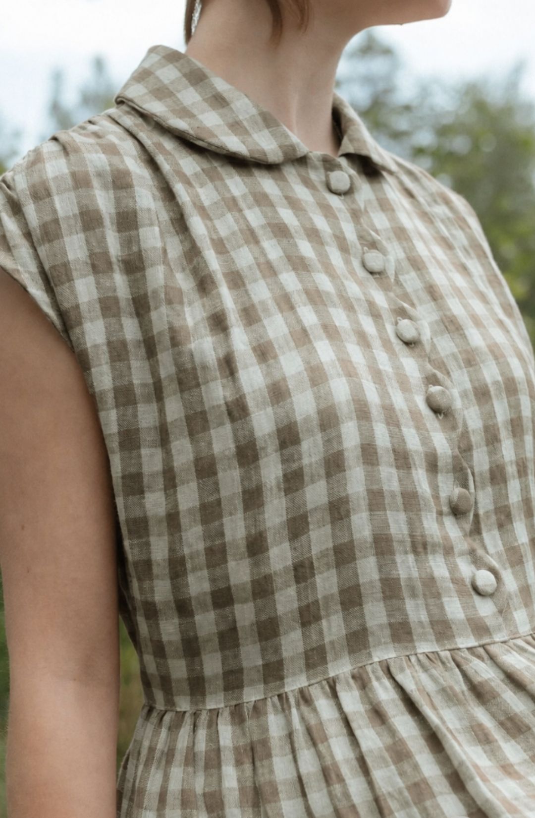 Close-up of a sleeveless checkered dress with buttons on a blurred natural background