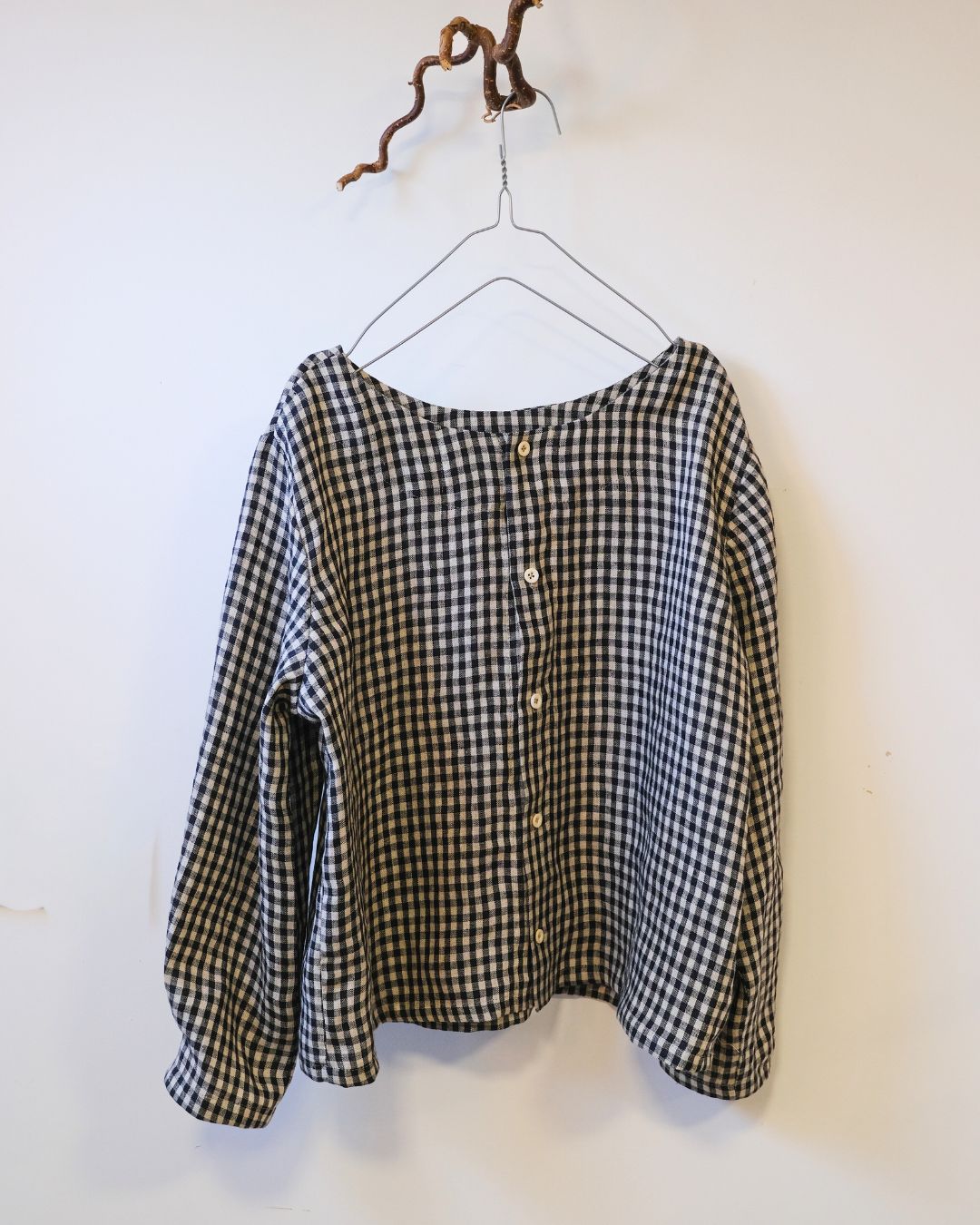 Black and grey check top on a hanger with buttoned back against a white background.