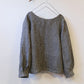 Black and grey check top with round neck, long sleeves against a white background.