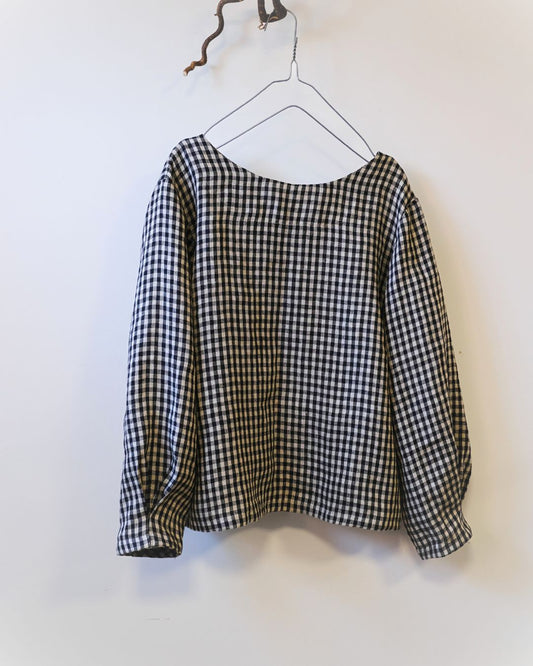 Black and grey check top with round neck, long sleeves against a white background.