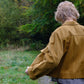Person wearing a brown jacket walking on a path with greenery in the background