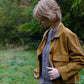 Woman wearing a brown jacket in a natural setting with greenery.