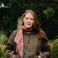 model wearing  green hornbeam jacket and red patterned scarf standing in a garden.