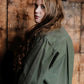 Woman wearing a green jacket - showing back pleat  against a wooden wall