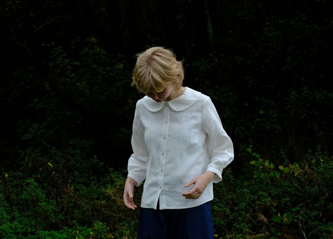 person standing by forest wearing a white linen blouse