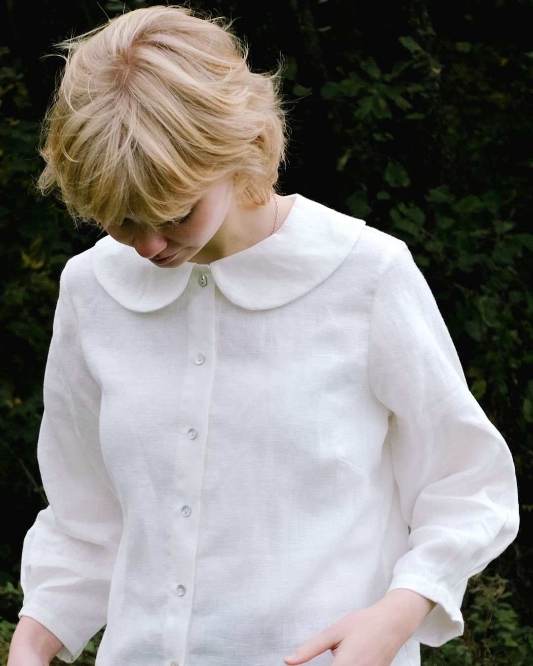 Person wearing a white shirt with a Peter Pan collar against a dark background