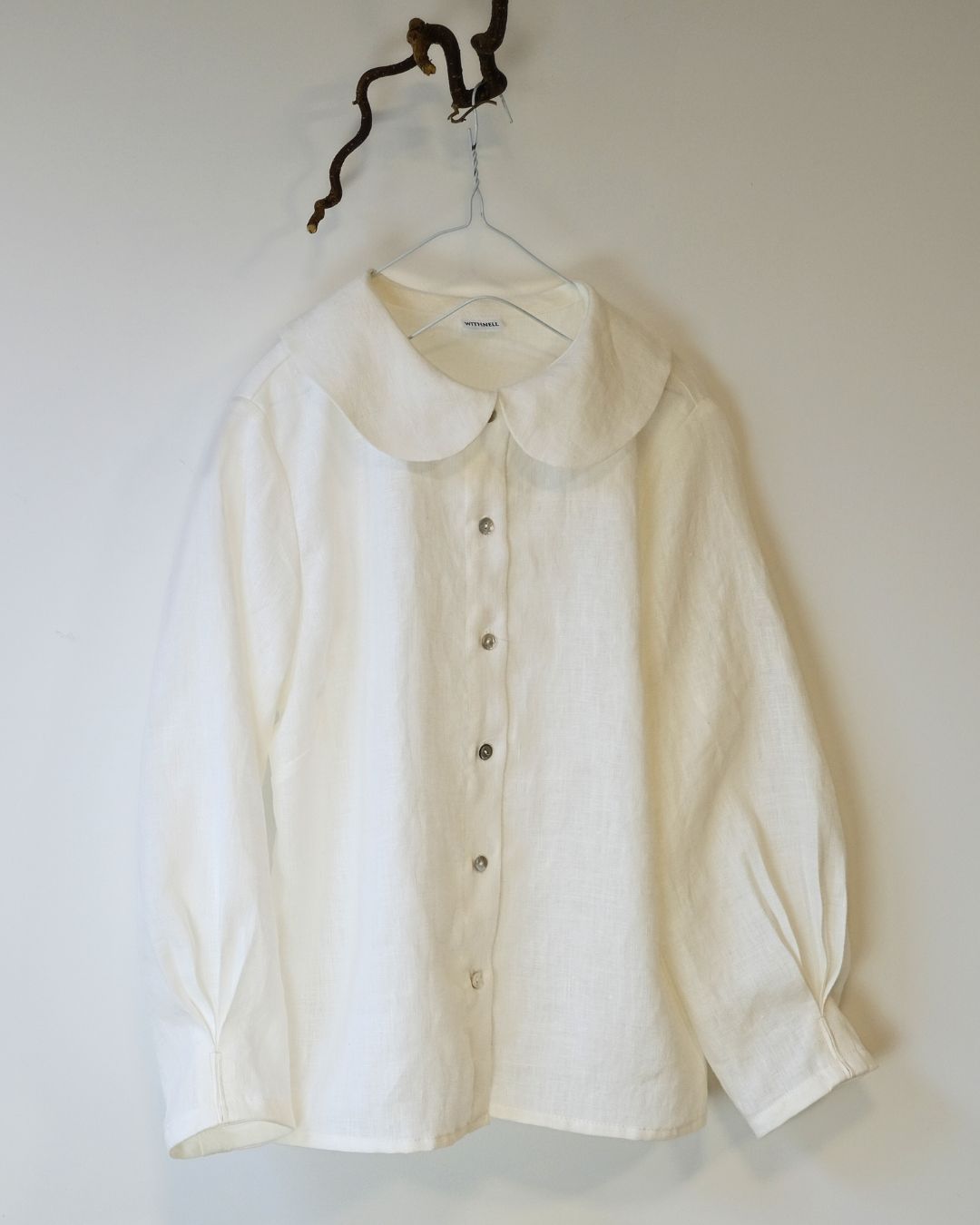 White blouse on a hanger against a plain white background